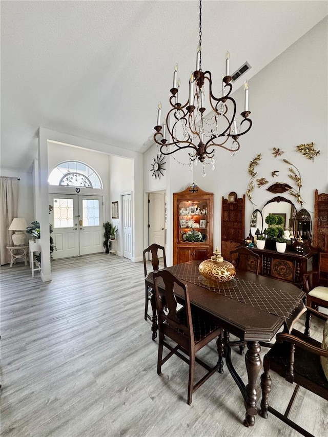 dining area with a notable chandelier, high vaulted ceiling, and light hardwood / wood-style floors