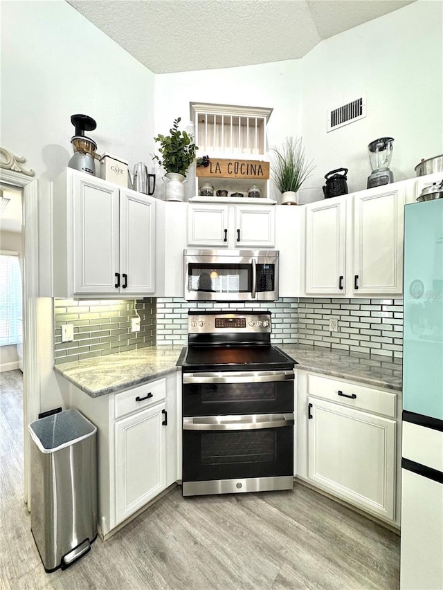 kitchen featuring lofted ceiling, white cabinetry, light hardwood / wood-style flooring, and appliances with stainless steel finishes