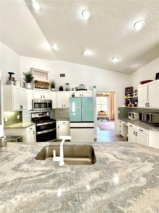 kitchen featuring stainless steel appliances, white cabinetry, lofted ceiling, and sink