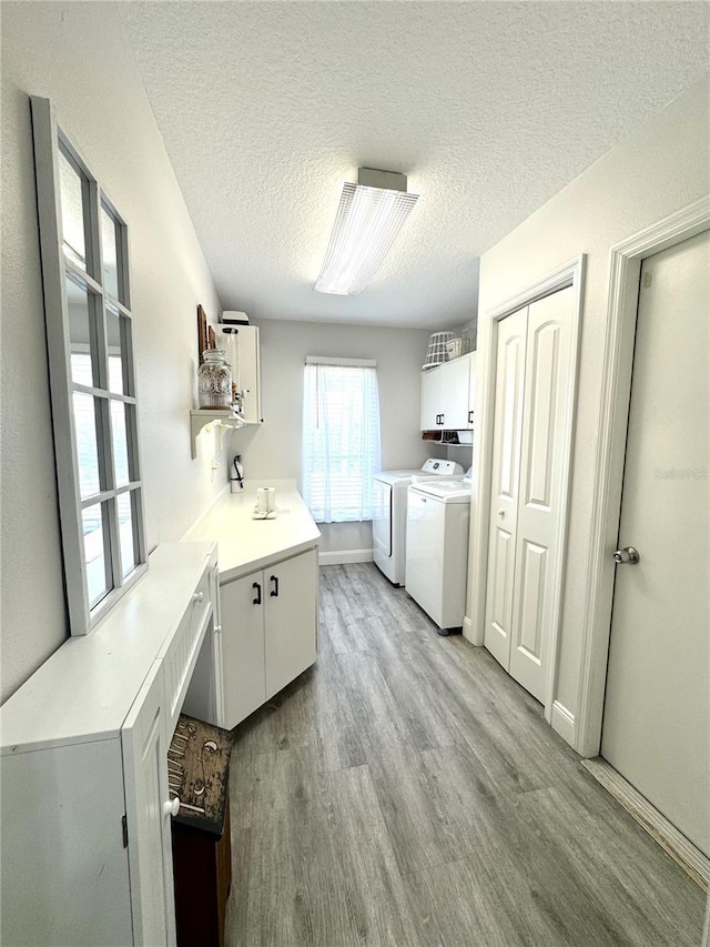 laundry area with cabinets, washing machine and dryer, a textured ceiling, and light wood-type flooring