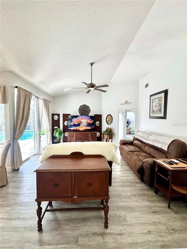 living room with ceiling fan, lofted ceiling, a textured ceiling, and light wood-type flooring