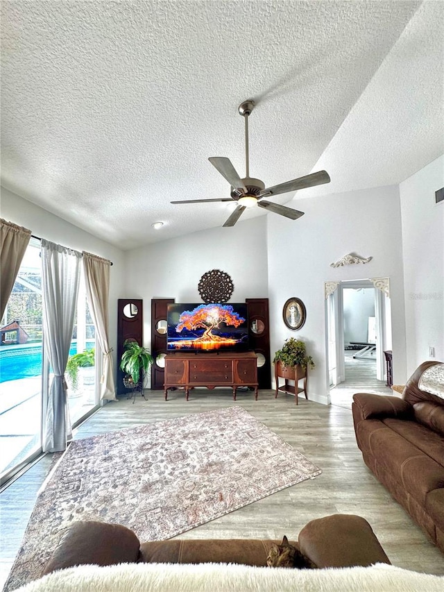 living room featuring ceiling fan, vaulted ceiling, a textured ceiling, and light wood-type flooring