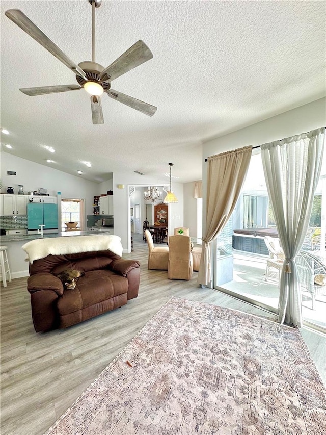 living room with ceiling fan with notable chandelier, light hardwood / wood-style floors, vaulted ceiling, and a textured ceiling