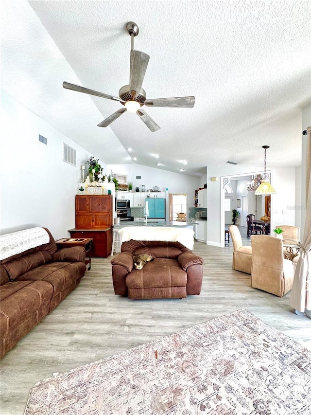 living room featuring ceiling fan with notable chandelier, vaulted ceiling, a textured ceiling, and light wood-type flooring