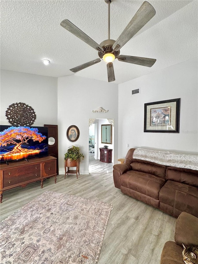 living room featuring ceiling fan, a textured ceiling, and light wood-type flooring