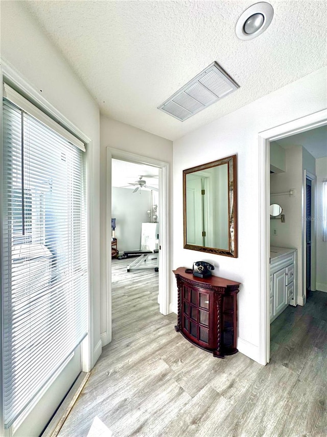 hallway with a textured ceiling and light hardwood / wood-style flooring