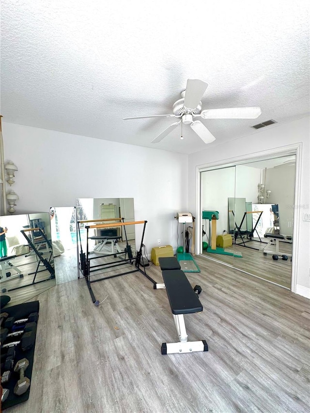 exercise room featuring ceiling fan, hardwood / wood-style floors, and a textured ceiling