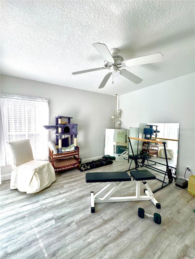 workout room featuring ceiling fan, light hardwood / wood-style floors, and a textured ceiling