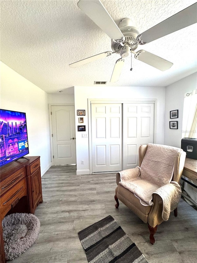 living area with ceiling fan, a textured ceiling, and light wood-type flooring