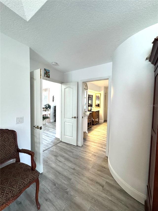 hallway with a textured ceiling and light hardwood / wood-style flooring