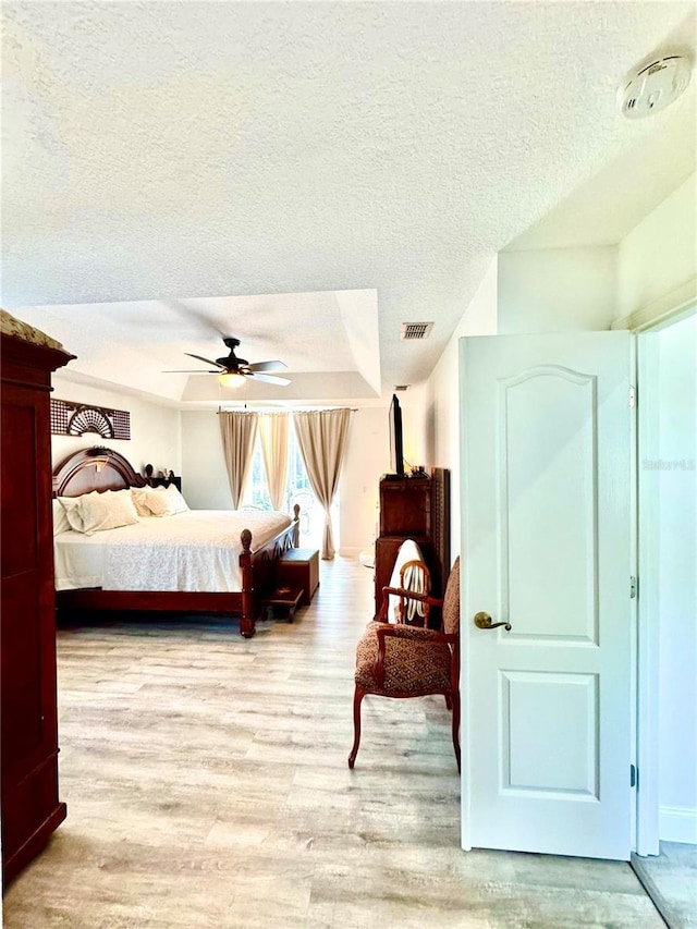 bedroom with a textured ceiling, light hardwood / wood-style flooring, and ceiling fan