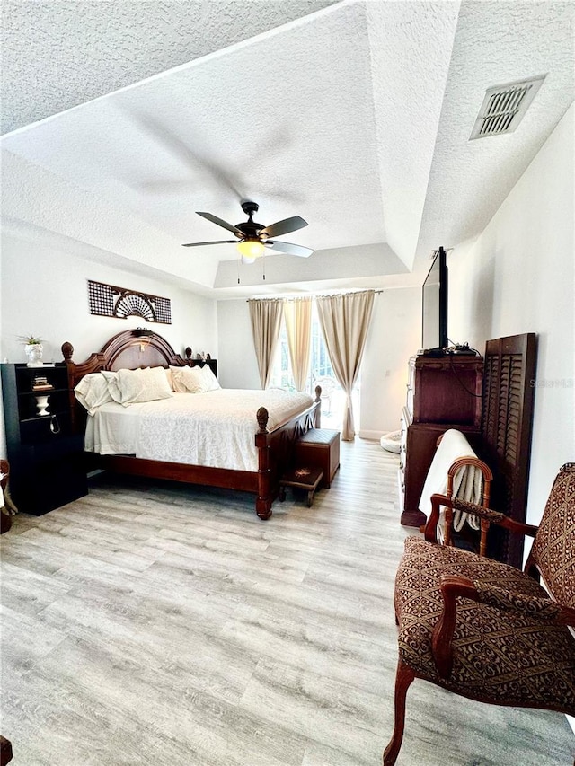 bedroom featuring a tray ceiling, a textured ceiling, light hardwood / wood-style floors, and ceiling fan