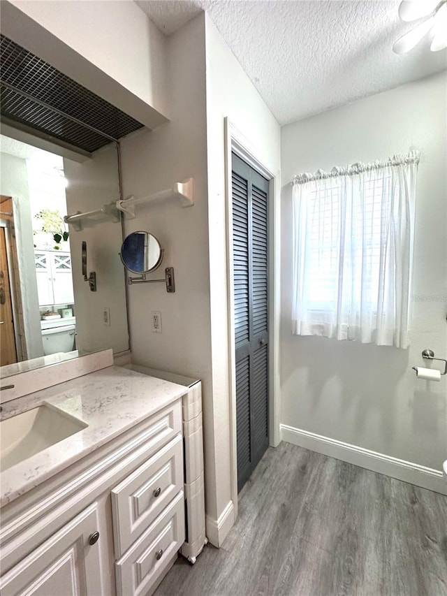 bathroom featuring baseboards, toilet, vanity, wood finished floors, and a textured ceiling