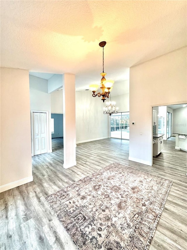 unfurnished dining area with baseboards, a notable chandelier, wood finished floors, and a textured ceiling