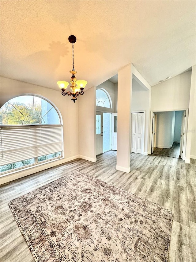 spare room featuring lofted ceiling, an inviting chandelier, wood finished floors, and a healthy amount of sunlight