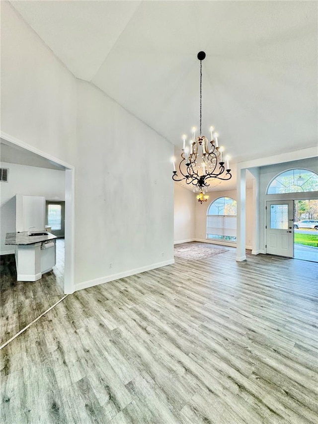 unfurnished dining area featuring wood finished floors, visible vents, baseboards, an inviting chandelier, and lofted ceiling