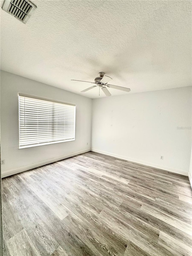 unfurnished room featuring ceiling fan, visible vents, baseboards, and wood finished floors