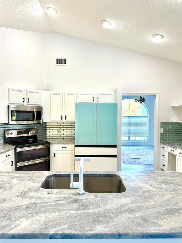 kitchen with visible vents, light stone countertops, appliances with stainless steel finishes, white cabinets, and a sink