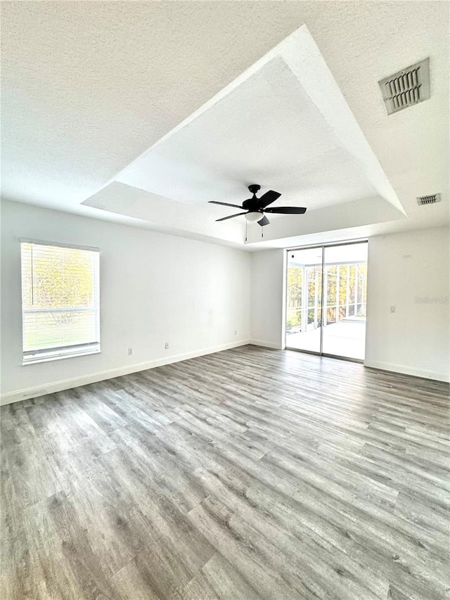 empty room with a tray ceiling, a textured ceiling, visible vents, and wood finished floors