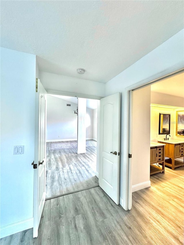 hall with baseboards, a textured ceiling, and light wood-style floors