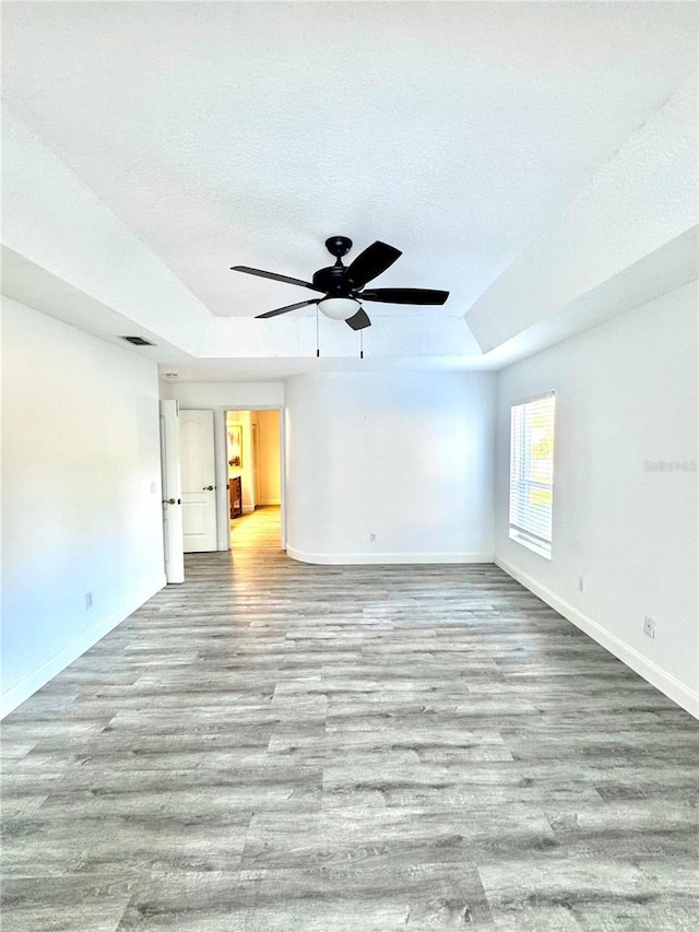 spare room featuring a tray ceiling, wood finished floors, baseboards, and a textured ceiling