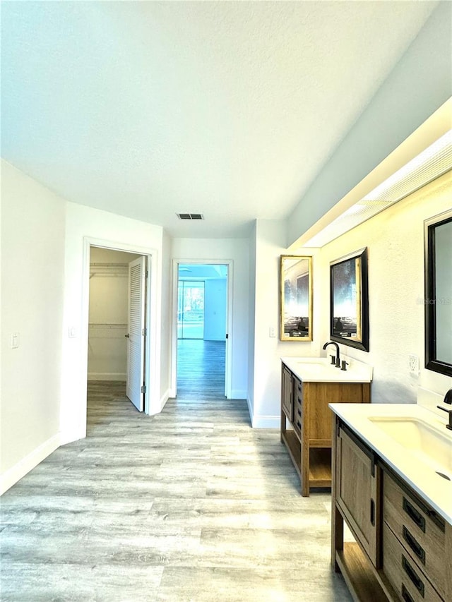 bathroom featuring two vanities, wood finished floors, baseboards, and a sink