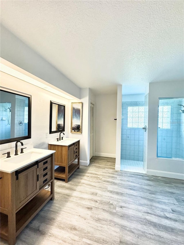 bathroom featuring a sink, a textured ceiling, wood finished floors, and a tile shower