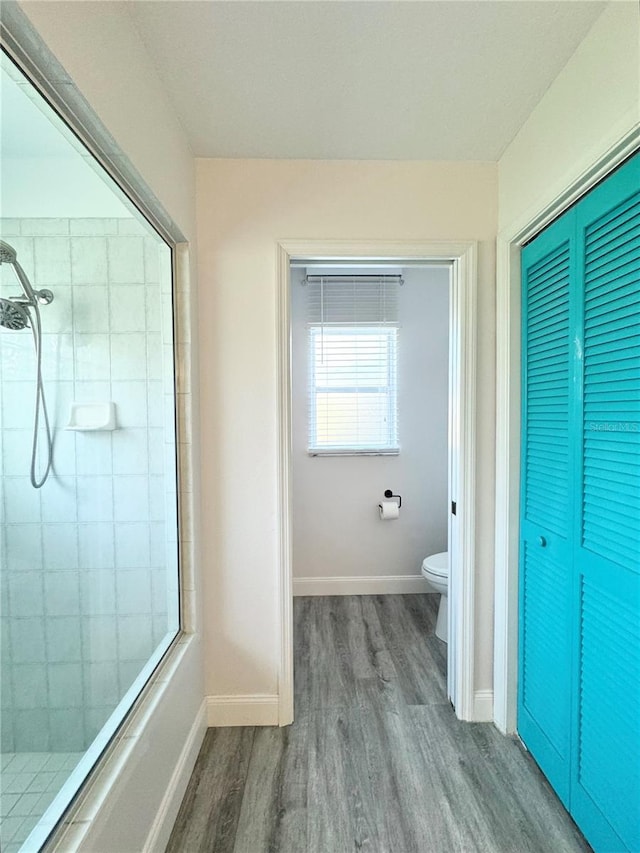 full bath featuring baseboards, toilet, wood finished floors, and a tile shower