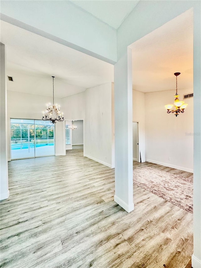 empty room with baseboards, wood finished floors, visible vents, and a chandelier