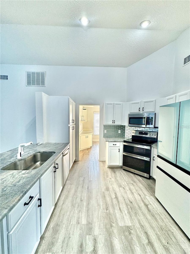 kitchen with visible vents, a sink, white cabinets, light wood-style floors, and appliances with stainless steel finishes