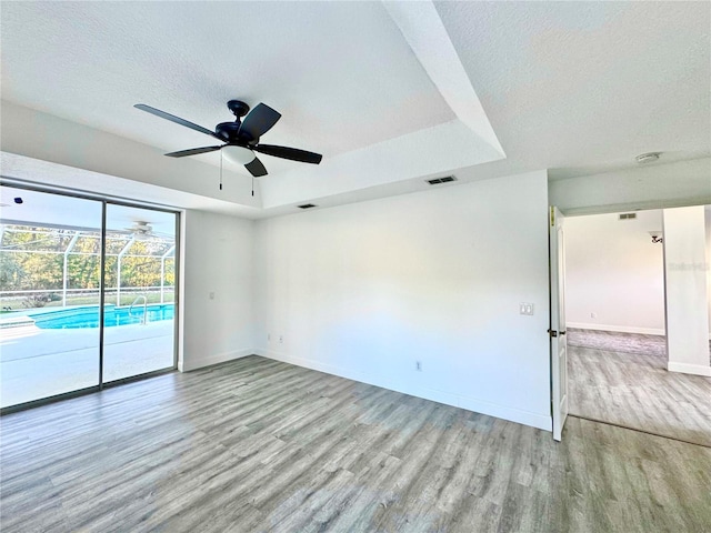 empty room featuring visible vents, a textured ceiling, wood finished floors, baseboards, and a raised ceiling