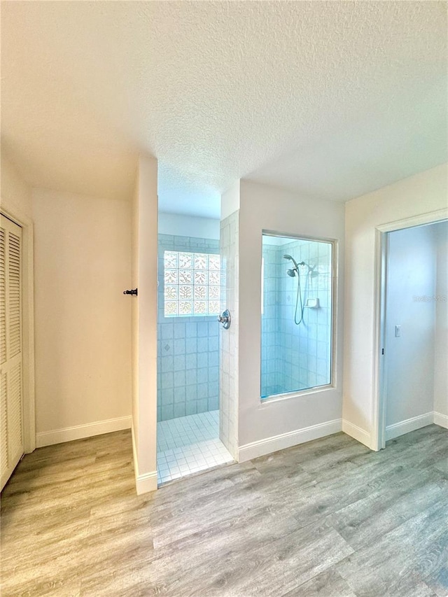 bathroom with baseboards, a textured ceiling, wood finished floors, and a tile shower