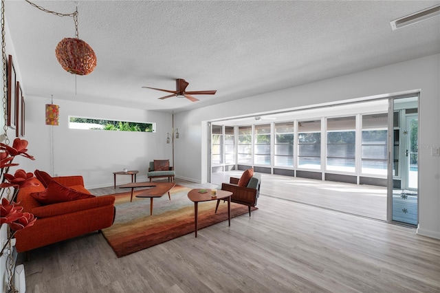 living room with a wealth of natural light, a textured ceiling, ceiling fan, and light hardwood / wood-style flooring