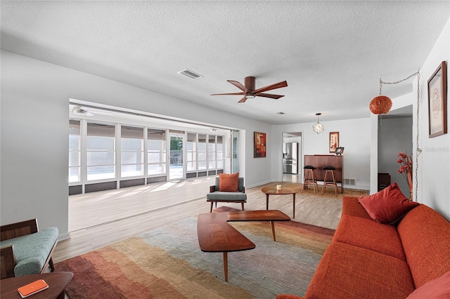 living room featuring ceiling fan, light hardwood / wood-style floors, and a textured ceiling