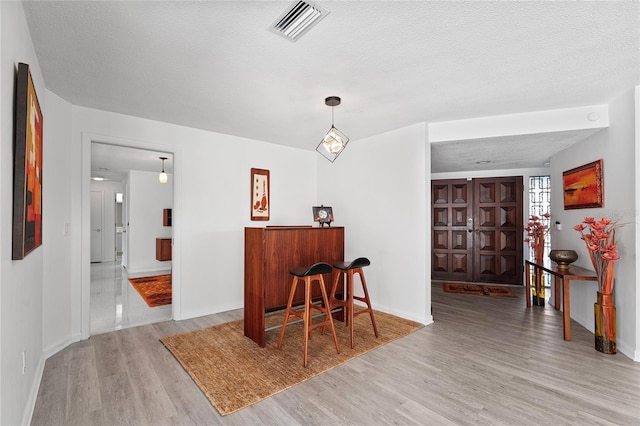 bar with decorative light fixtures, light hardwood / wood-style floors, and a textured ceiling