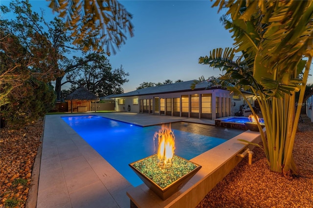 pool at dusk with a patio area and an in ground hot tub