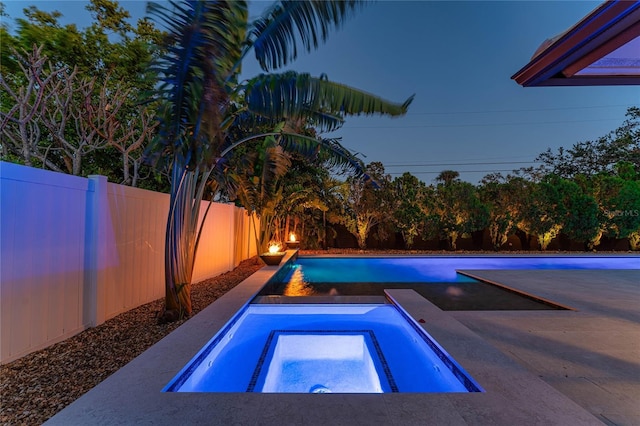 pool at dusk featuring an in ground hot tub