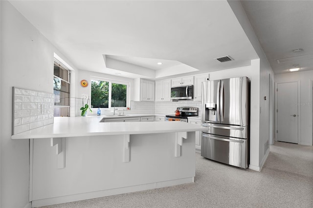 kitchen with appliances with stainless steel finishes, a kitchen breakfast bar, kitchen peninsula, white cabinets, and a raised ceiling