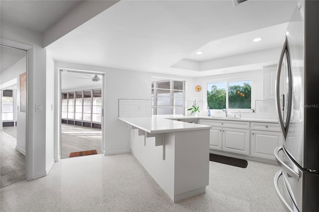 kitchen with stainless steel fridge, a breakfast bar, white cabinetry, decorative backsplash, and a raised ceiling