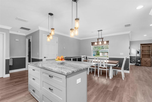 kitchen with light stone countertops, a center island, light hardwood / wood-style flooring, pendant lighting, and white cabinets