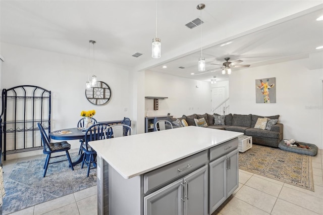 kitchen with light tile patterned floors, gray cabinets, ceiling fan, hanging light fixtures, and a kitchen island