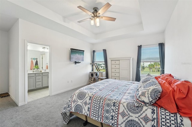 bedroom with multiple windows, ensuite bath, light colored carpet, and a raised ceiling