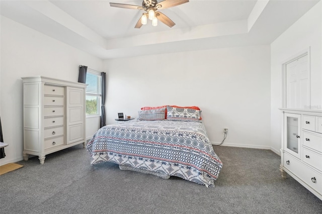 bedroom with ceiling fan, a raised ceiling, and dark carpet