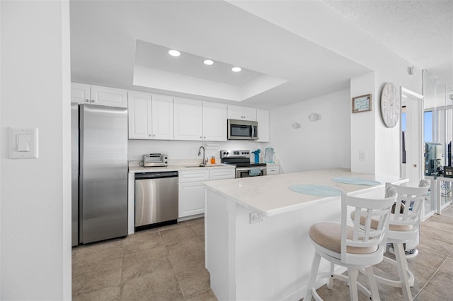 kitchen with white cabinetry, stainless steel appliances, kitchen peninsula, a tray ceiling, and a breakfast bar