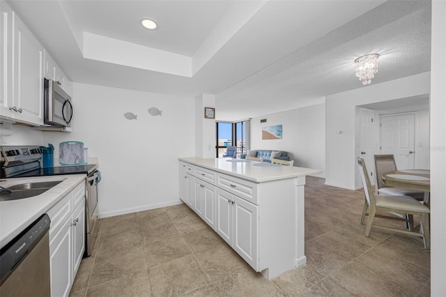 kitchen with white cabinetry, kitchen peninsula, a textured ceiling, a tray ceiling, and appliances with stainless steel finishes