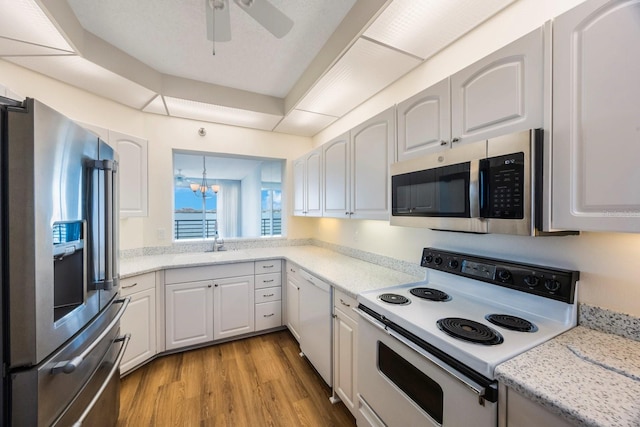 kitchen with stainless steel appliances, light stone countertops, light hardwood / wood-style floors, white cabinets, and ceiling fan with notable chandelier