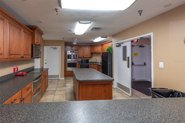 kitchen featuring light tile patterned floors, sink, black appliances, a textured ceiling, and a kitchen island