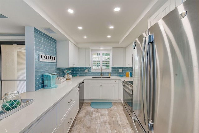 kitchen with decorative backsplash, appliances with stainless steel finishes, sink, white cabinets, and light hardwood / wood-style floors