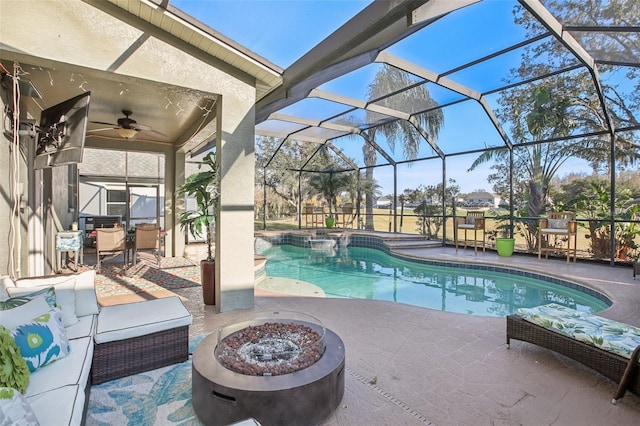 view of pool featuring a patio area, ceiling fan, glass enclosure, and an outdoor fire pit