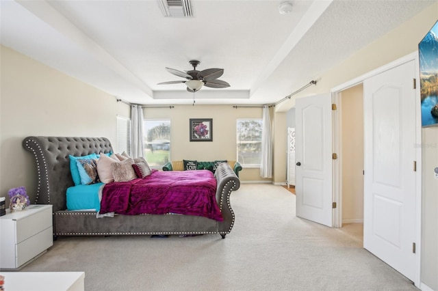 carpeted bedroom with ceiling fan, a raised ceiling, and multiple windows